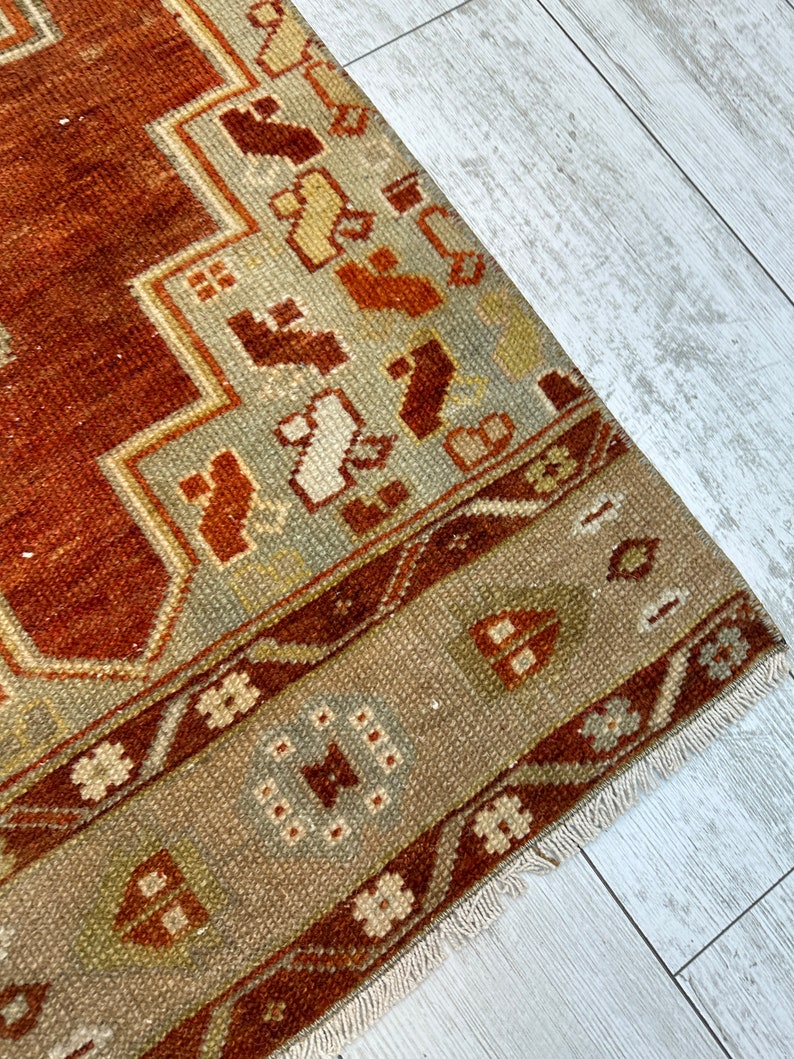 May include: A vintage rug with a brown, beige, and white geometric pattern. The rug has a fringe border and is made of wool.