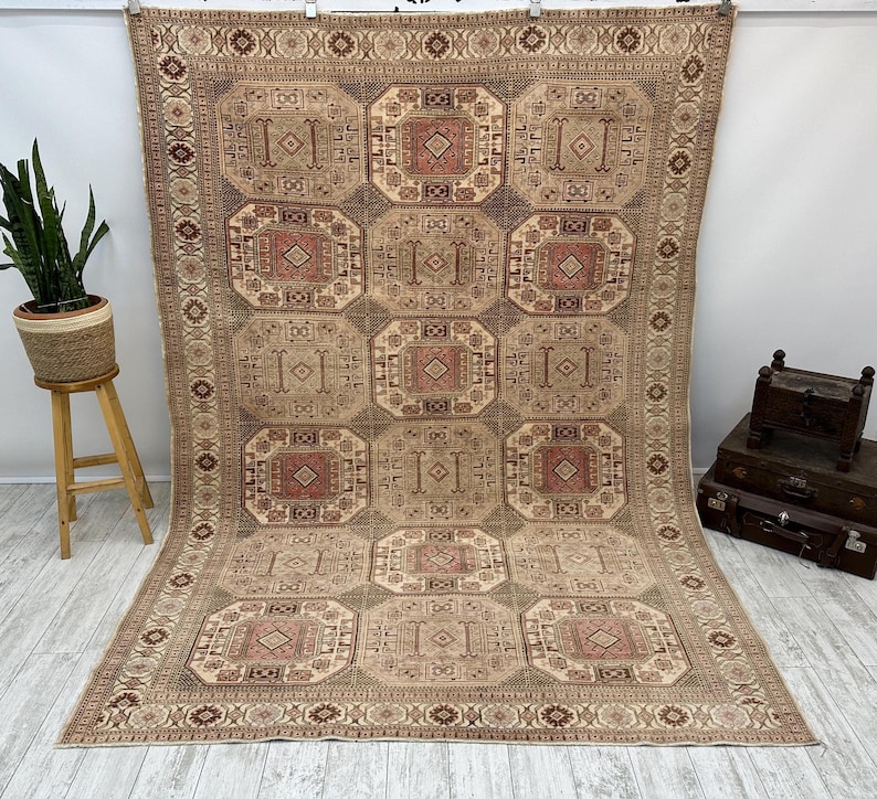 May include: A beige and brown patterned rug with a geometric design. The rug has a central medallion with a repeating pattern of squares and diamonds.