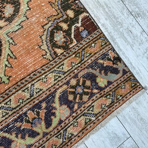 May include: A vintage rug with a faded orange background and intricate floral patterns in shades of green, blue, and black. The rug has a fringed edge.