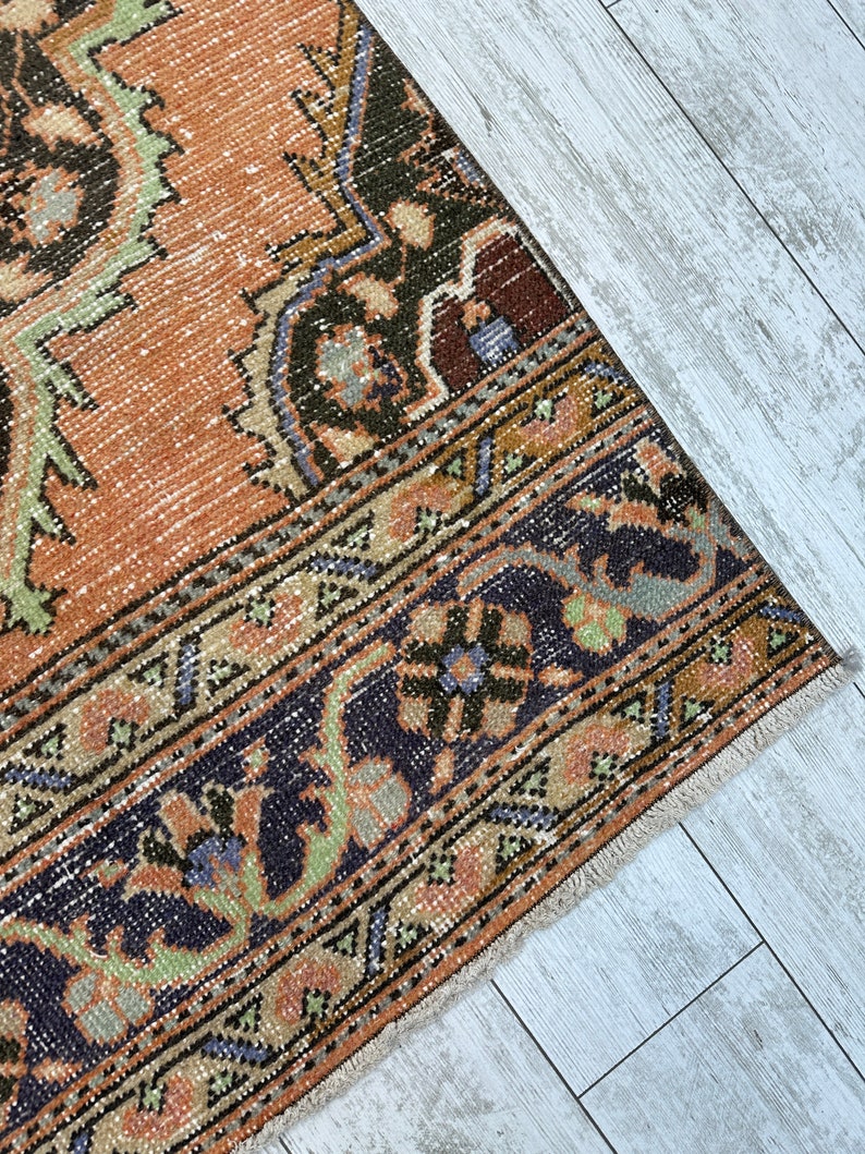 May include: A vintage rug with a faded orange background and intricate floral patterns in shades of green, blue, and black. The rug has a fringed edge.