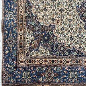 May include: A vintage Persian rug with a blue and cream color scheme. The rug features intricate floral and geometric patterns throughout. The rug has a fringe border.