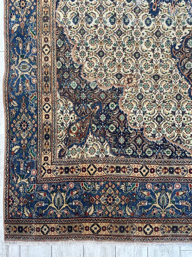 May include: A vintage Persian rug with a blue and cream color scheme. The rug features intricate floral and geometric patterns throughout. The rug has a fringe border.