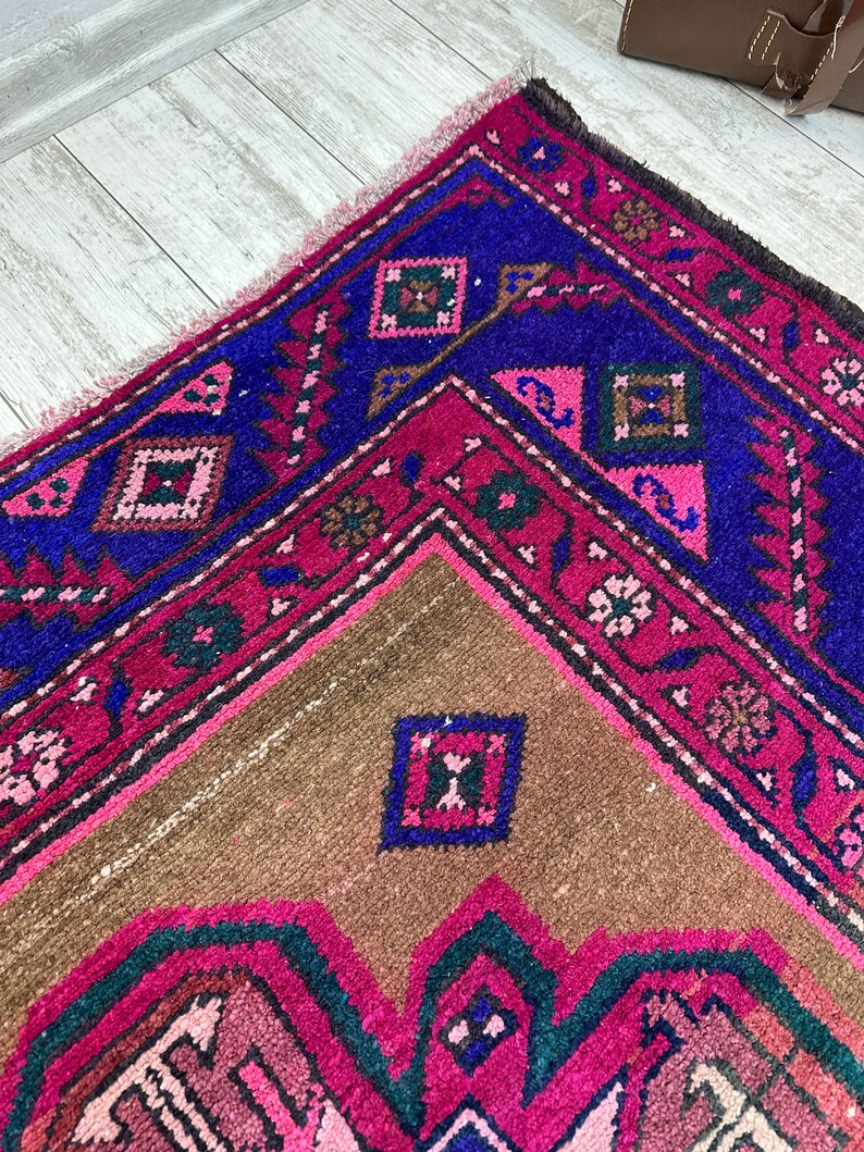 May include: A vintage Turkish rug with a geometric pattern in shades of pink, blue, and brown. The rug has a fringed edge and is woven with intricate details.