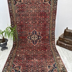 May include: A vintage Persian rug with a red background and intricate floral patterns in shades of blue, green, and ivory. The rug has a central medallion and a border with a repeating geometric design.
