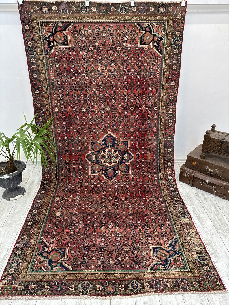 May include: A vintage Persian rug with a red background and intricate floral patterns in shades of blue, green, and ivory. The rug has a central medallion and a border with a repeating geometric design.