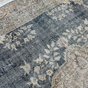 K&ouml;nnte beinhalten: Ein runder Vintage-Teppich mit dunkelblauem Hintergrund und einem verblassten beigefarbenen Blumenmuster. Der Teppich hat einen abgenutzten Look und einen abgenutzten Rand.