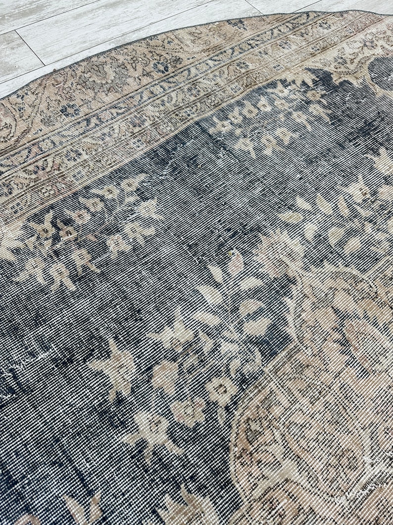 K&ouml;nnte beinhalten: Ein runder Vintage-Teppich mit dunkelblauem Hintergrund und einem verblassten beigefarbenen Blumenmuster. Der Teppich hat einen abgenutzten Look und einen abgenutzten Rand.