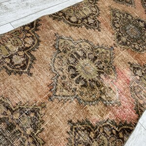Puede incluir: Una alfombra vintage con un esquema de color rosa y marr&oacute;n descolorido. La alfombra tiene un dise&ntilde;o persa tradicional con intrincados patrones florales.