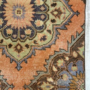 May include: A vintage rug with a faded, peach-colored background and intricate, multi-colored floral patterns. The rug has a distressed, worn look with shades of brown, green, blue, and purple.