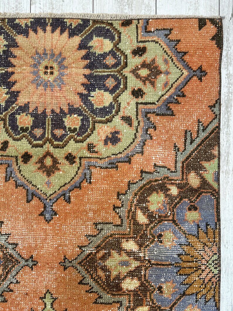 May include: A vintage rug with a faded, peach-colored background and intricate, multi-colored floral patterns. The rug has a distressed, worn look with shades of brown, green, blue, and purple.