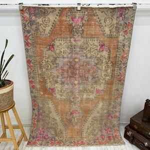 May include: A vintage rug with a faded orange background and intricate floral patterns in shades of pink, beige, and grey. The rug has a distressed look and is perfect for adding a touch of bohemian style to any room.
