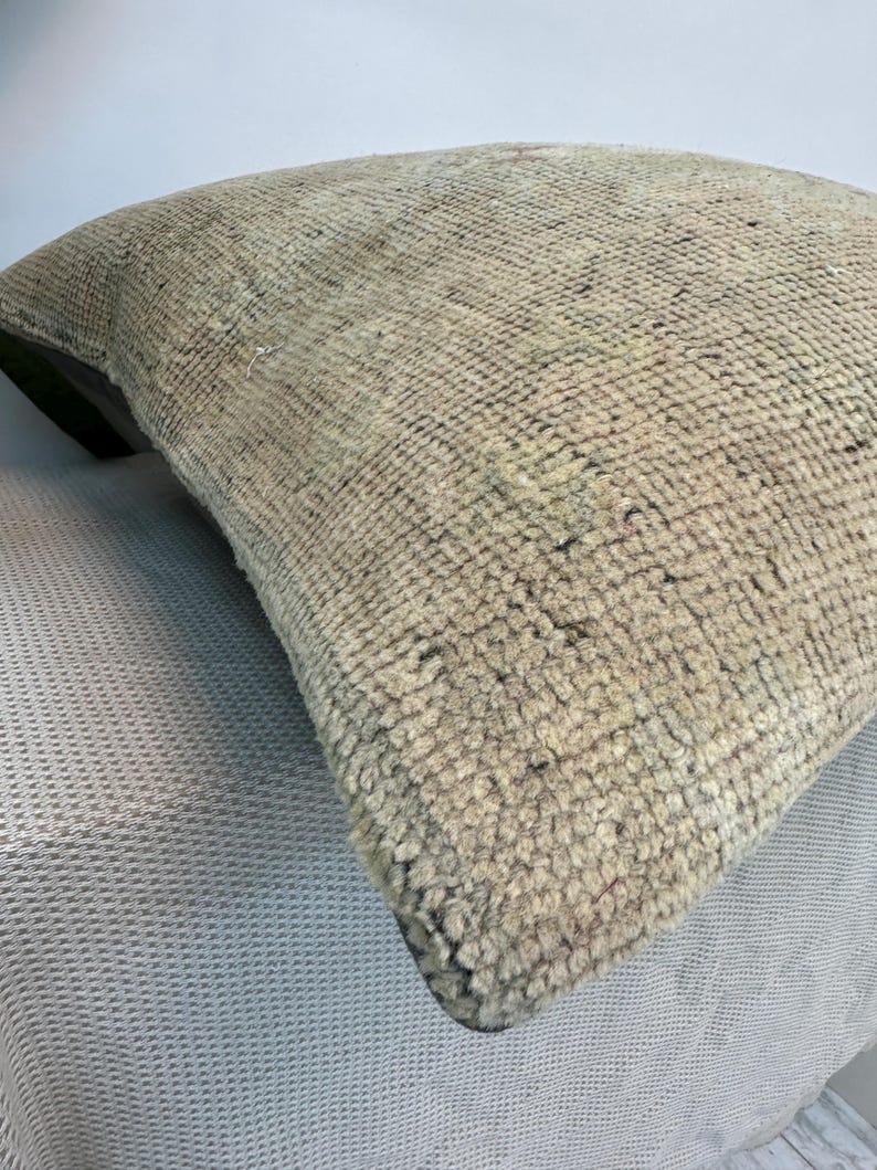 May include: A square throw pillow featuring a thick, hand-knotted wool pile in a neutral beige and tan color palette. The textured surface displays a dense, looped weave with subtle variations in tone, creating a tactile and uniform appearance.