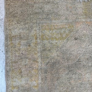 May include: A close-up of a beige rug with a subtle pattern. The rug has a frayed edge and a soft, textured surface.