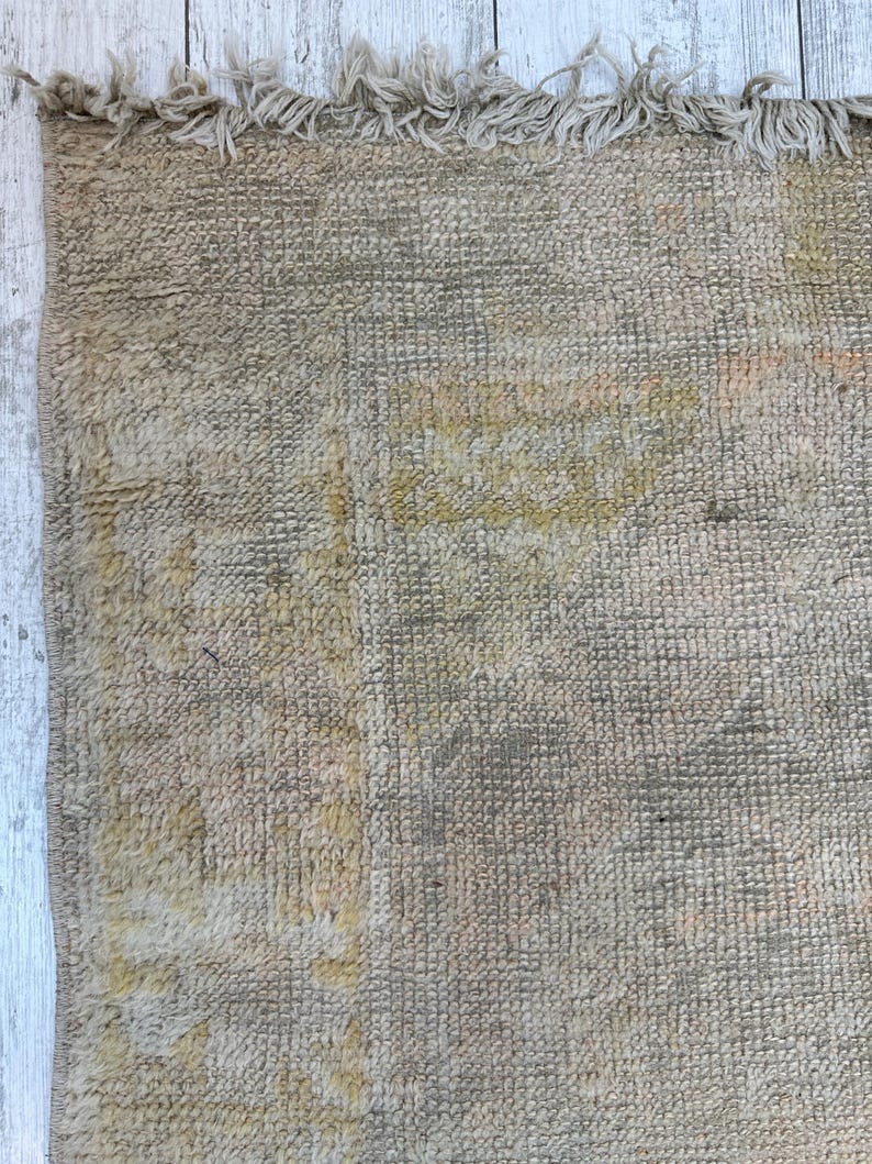 May include: A close-up of a beige rug with a subtle pattern. The rug has a frayed edge and a soft, textured surface.