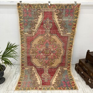 May include: A vintage rug with a faded pink, red, and green floral pattern. The rug has a distressed look and is perfect for adding a touch of bohemian style to your home.