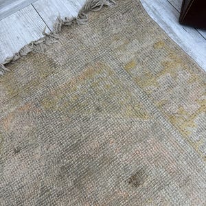 May include: A close-up of a beige woven rug with a frayed edge. The rug has a subtle pattern and a worn, vintage look.
