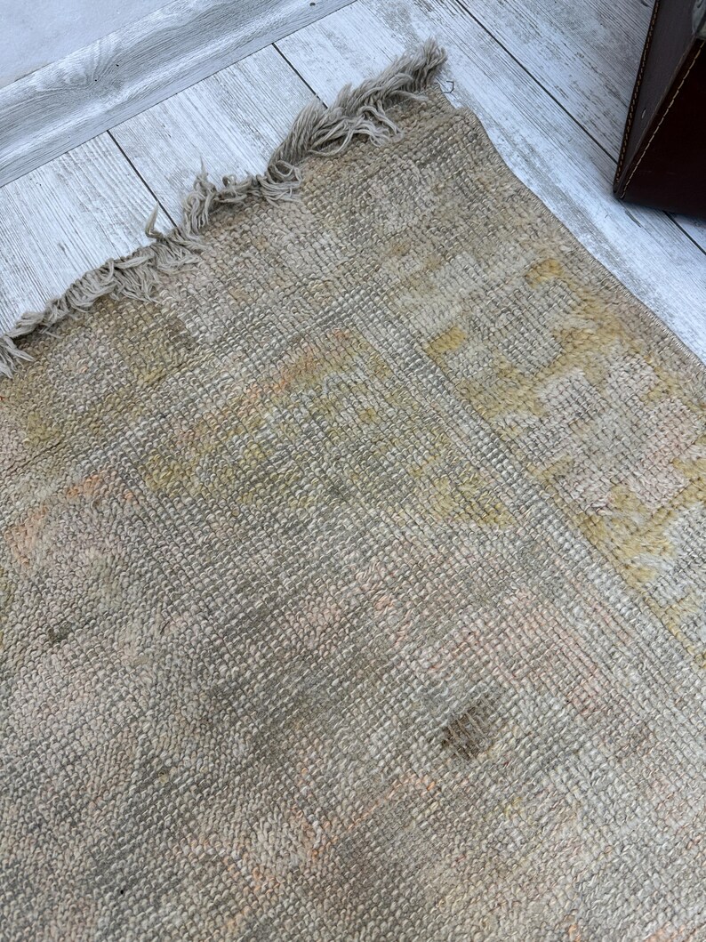 May include: A close-up of a beige woven rug with a frayed edge. The rug has a subtle pattern and a worn, vintage look.