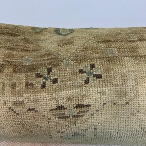 May include: A rectangular throw cushion featuring a woven texture in shades of beige and tan. The surface displays a repeating pattern of small, dark brown floral motifs and subtle light blue accents integrated into the fabric's weave.