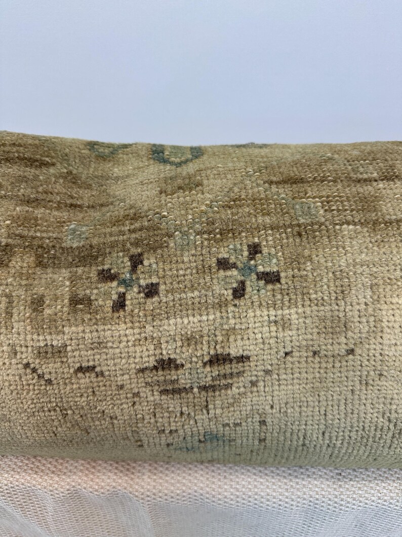 May include: A rectangular throw cushion featuring a woven texture in shades of beige and tan. The surface displays a repeating pattern of small, dark brown floral motifs and subtle light blue accents integrated into the fabric's weave.