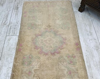 Puede incluir: Una alfombra rectangular con base de color beige, un medallón central y motivos florales en tonos suaves de verde salvia y rosa empolvado. La alfombra tiene una textura de pelo corto y está rematada con flecos cortos en ambos extremos.