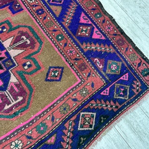 May include: A vintage rug with a brown background and a blue, pink, and green geometric pattern. The rug has a fringed edge.
