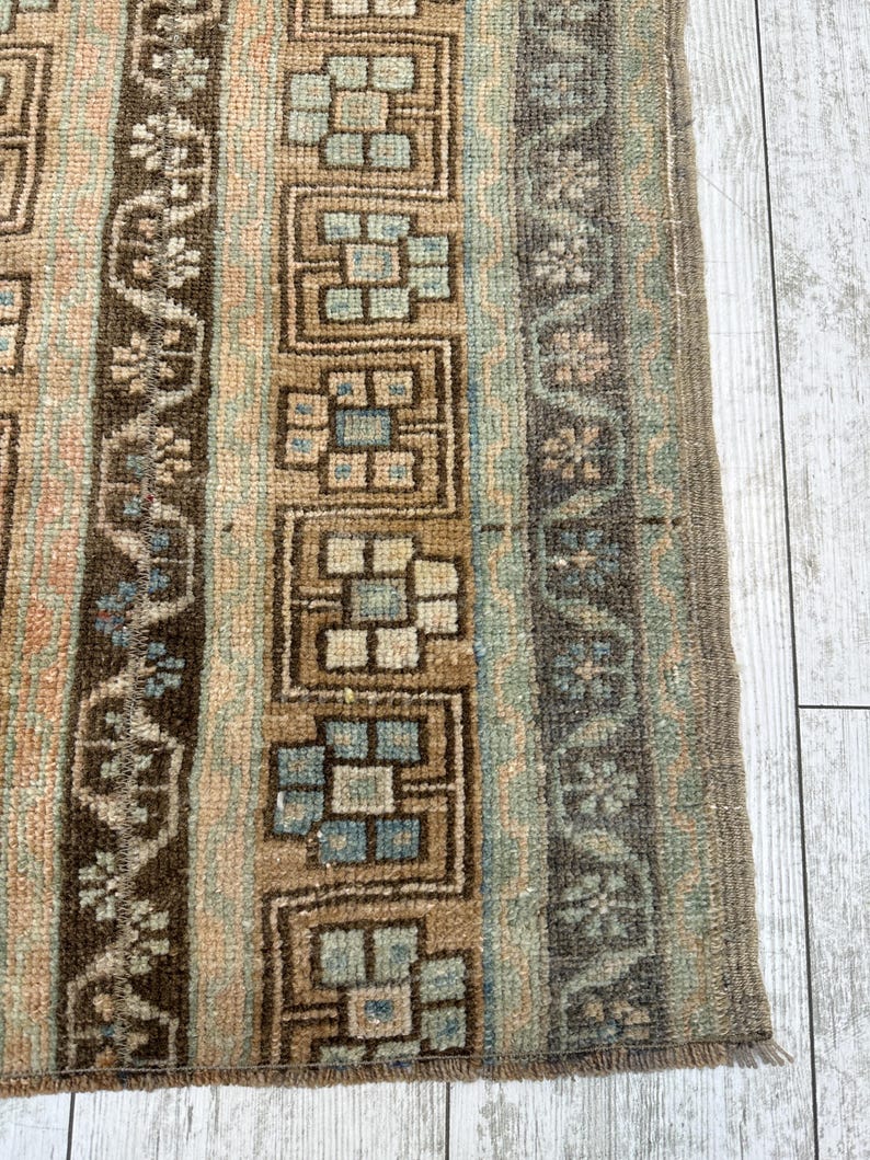 May include: Close-up of a section of a vintage rug with a geometric pattern. The rug features vertical stripes in shades of brown, beige, and blue-green. The design includes floral and block-like motifs, with a fringed edge.