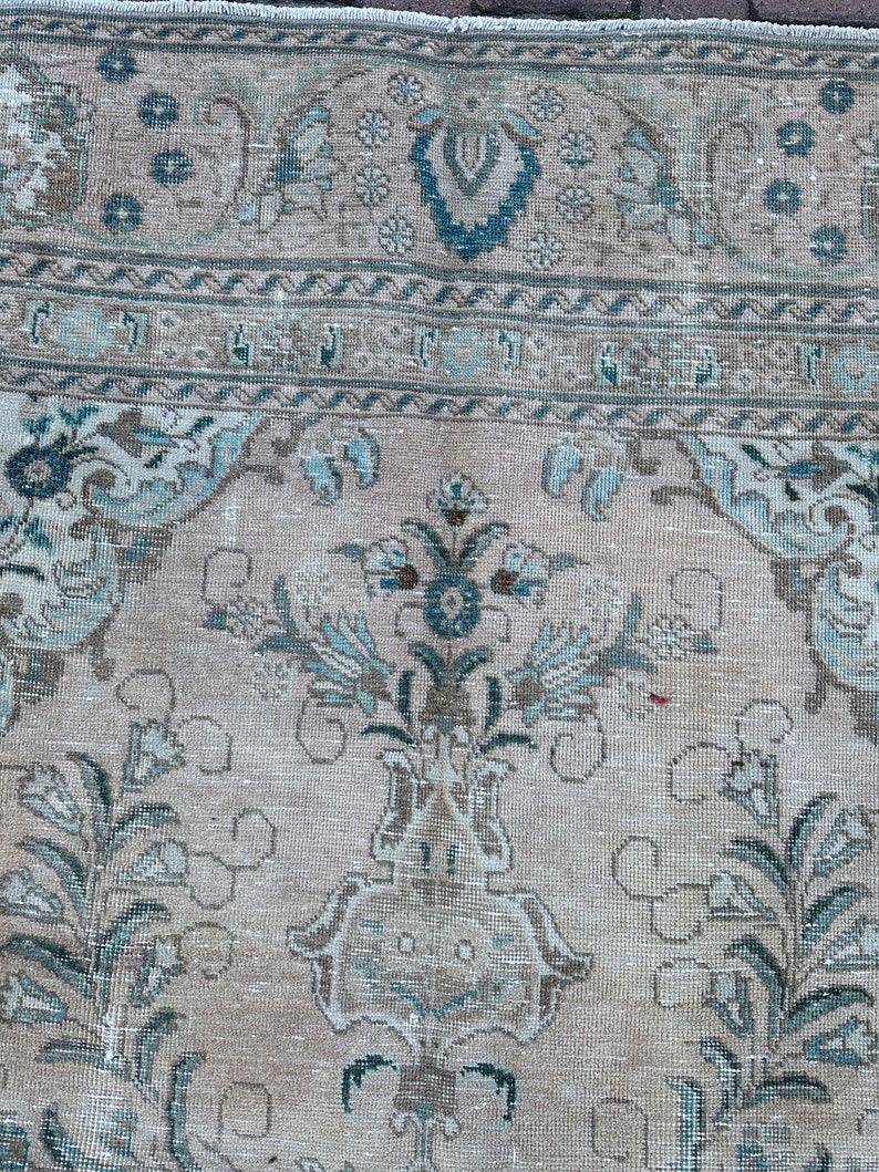 Puede incluir: Una alfombra vintage con fondo beige claro y un patr&oacute;n floral azul y blanco. La alfombra tiene un aspecto descolorido y est&aacute; hecha de un material suave y tejido.
