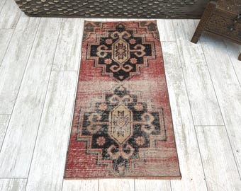 May include: A rectangular area rug featuring a faded red background with two prominent black and beige geometric medallions. The design includes intricate symmetrical patterns and a distressed texture throughout the woven fabric surface.