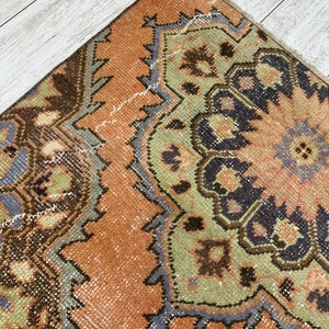 May include: A vintage rug with a brown, green, and blue geometric pattern. The rug has a faded, distressed look and is made of wool.
