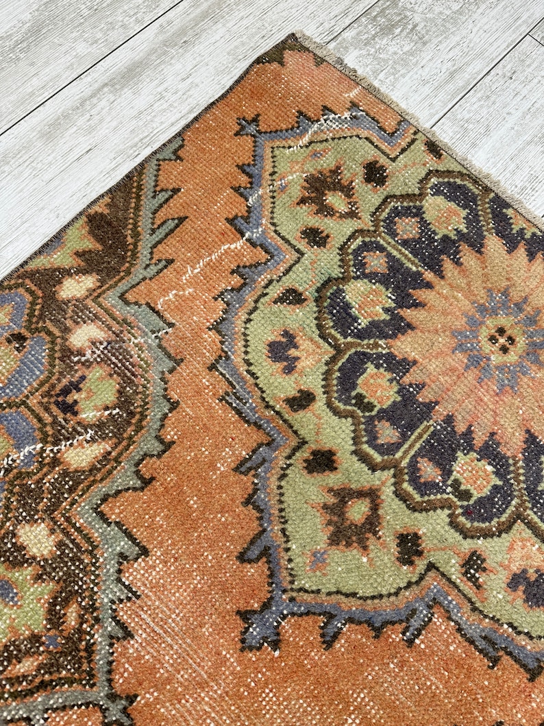 May include: A vintage rug with a brown, green, and blue geometric pattern. The rug has a faded, distressed look and is made of wool.