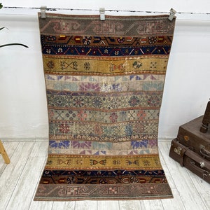 May include: A vintage Turkish kilim rug with a colourful geometric pattern in shades of brown, blue, red, and yellow. The rug has a faded, distressed look, giving it a unique character.