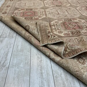 May include: A beige and pink vintage rug with a geometric pattern. The rug is folded in half and the edge is visible.