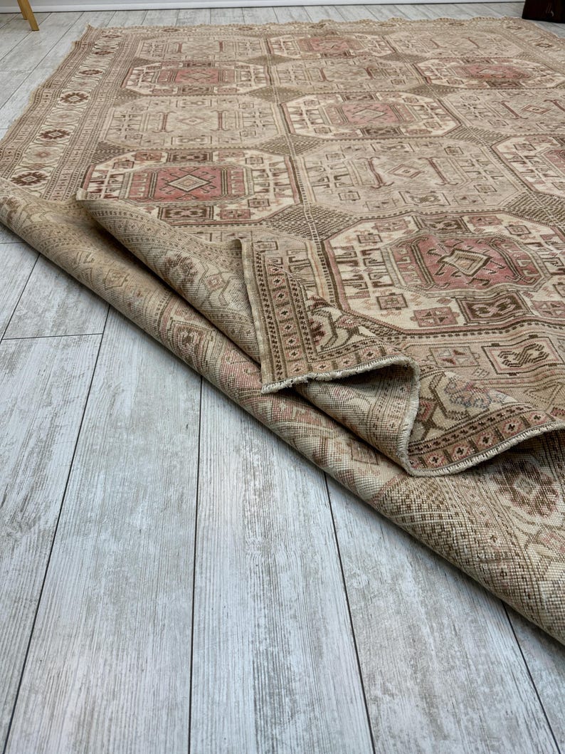 May include: A beige and pink vintage rug with a geometric pattern. The rug is folded in half and the edge is visible.