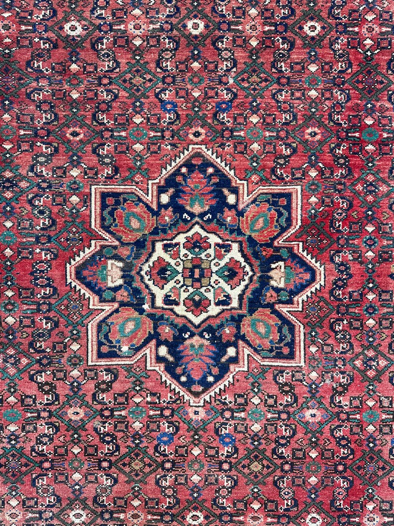 May include: A vintage Persian rug with a red background and a central medallion featuring a floral design in shades of blue, green, and white. The rug has a geometric border with intricate details.