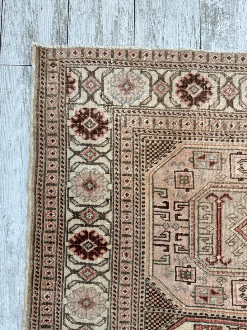 May include: A vintage rug with a cream background and intricate patterns in shades of brown, pink, and red. The rug features a central medallion with a geometric design and a border with repeating floral motifs.
