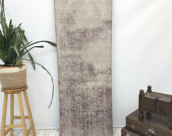 Puede incluir: Una alfombra pasillera larga y rectangular con un aspecto descolorido y desgastado, con una paleta de colores apagados en beige, topo y burdeos intenso. La alfombra muestra un intrincado patrón floral y geométrico en toda su superficie.