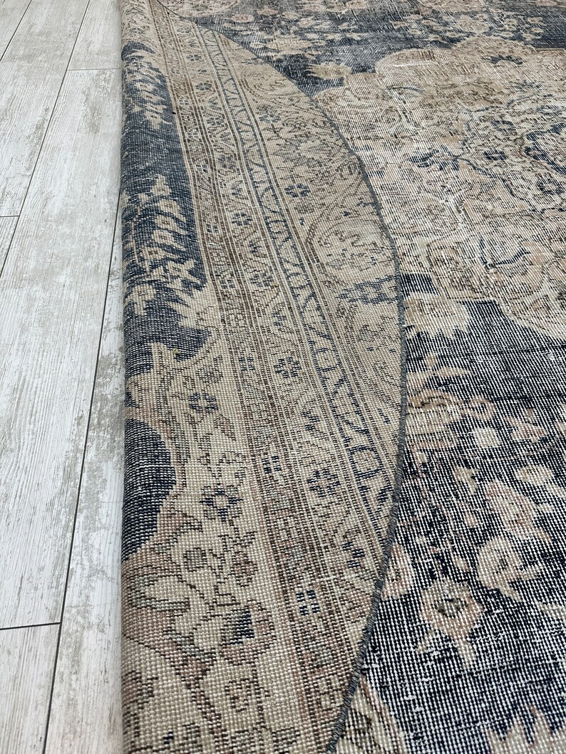 K&ouml;nnte beinhalten: Ein Vintage-Teppich mit einem verblassten, komplizierten Muster in Beige- und Schwarzt&ouml;nen. Der Teppich hat einen abgenutzten, verwitterten Look, der zu seinem Charakter und Charme beitr&auml;gt.