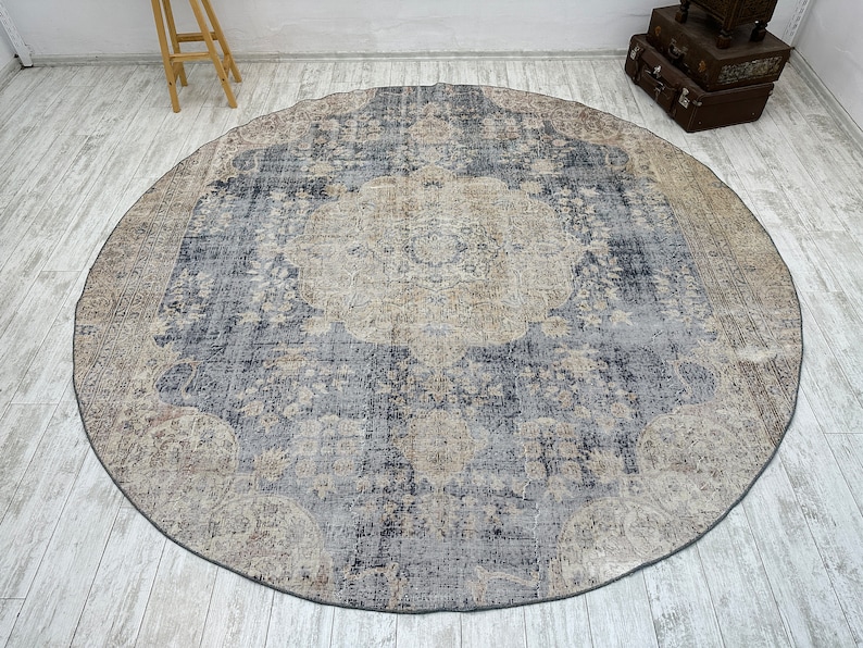K&ouml;nnte beinhalten: Ein runder, blau- und cremefarbener Teppich mit einem Blumenmuster. Der Teppich hat einen abgenutzten Look und ist aus einem weichen, gewebten Material gefertigt.