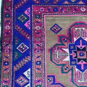 May include: A vintage rug with a geometric pattern in shades of pink, blue, green, and brown. The rug has a fringe border and is woven with intricate details.