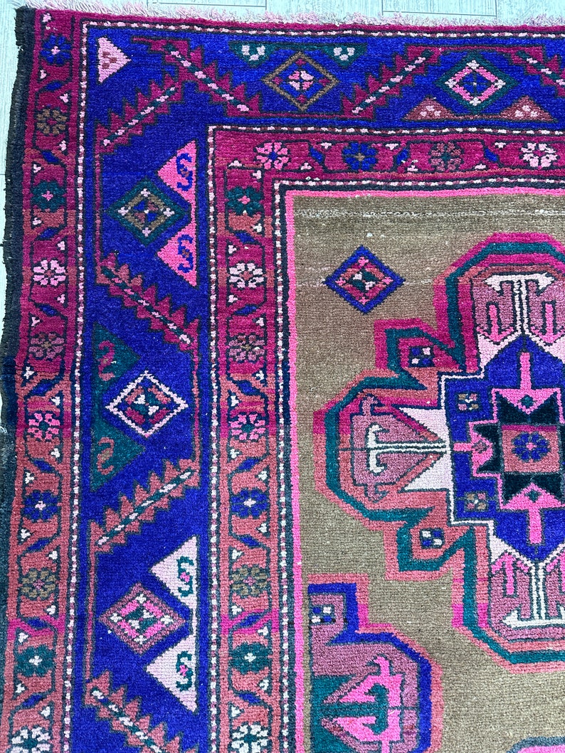 May include: A vintage rug with a geometric pattern in shades of pink, blue, green, and brown. The rug has a fringe border and is woven with intricate details.