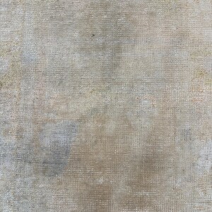 May include: A close-up of a beige canvas texture with a subtle woven pattern. The canvas has a slightly faded appearance with some light brown and gray discoloration.