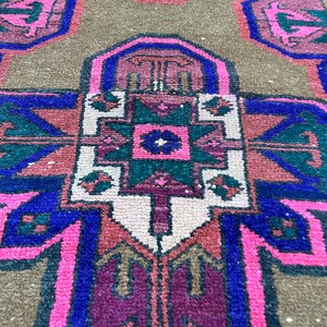 May include: A close-up of a colorful rug with intricate geometric patterns in shades of pink, blue, green, and brown. The rug has a traditional design with a central medallion and repeating motifs.