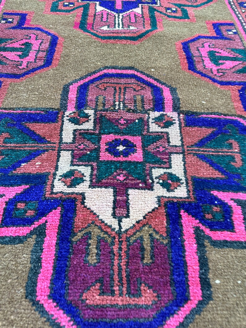 May include: A close-up of a colorful rug with intricate geometric patterns in shades of pink, blue, green, and brown. The rug has a traditional design with a central medallion and repeating motifs.