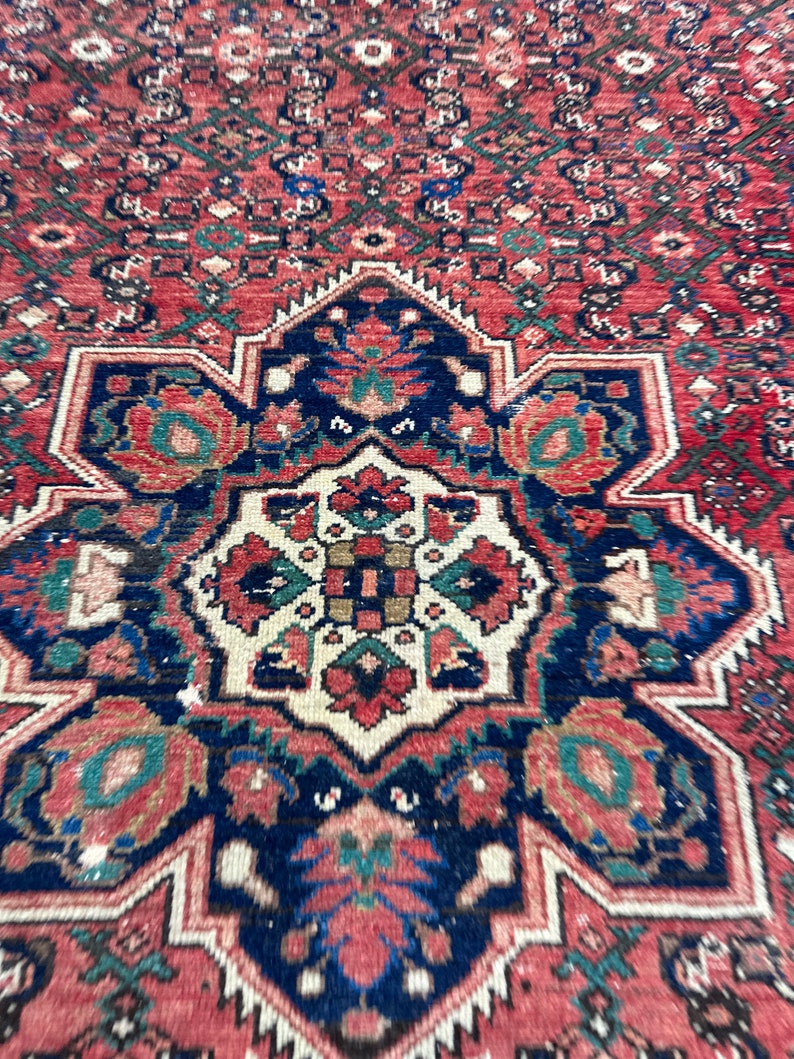 May include: A close-up of a red, blue, and green patterned rug with a central medallion. The rug has a traditional Persian design with intricate details.