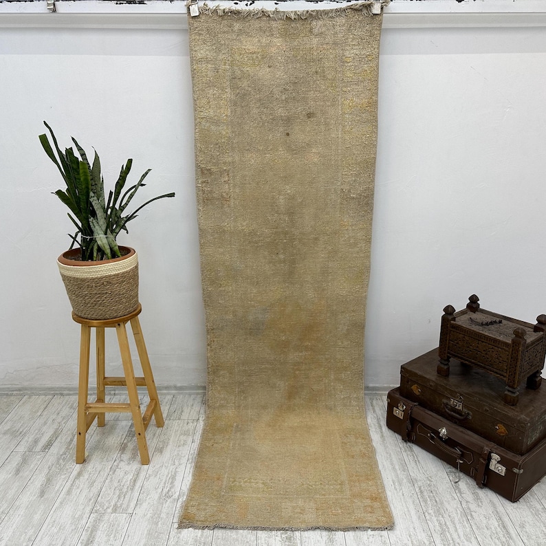 May include: A long, rectangular, off-white rug with a subtle woven texture. The rug is hanging on a white wall.