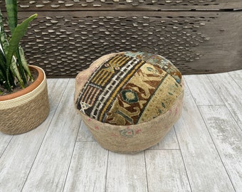 May include: A round, brown and beige patterned ottoman with a woven fabric cover. The ottoman is sitting on a light wood floor.