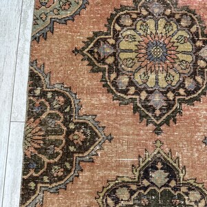 Puede incluir: Una alfombra vintage con un fondo rosa descolorido y intrincados patrones florales en tonos de verde, marr&oacute;n y azul.