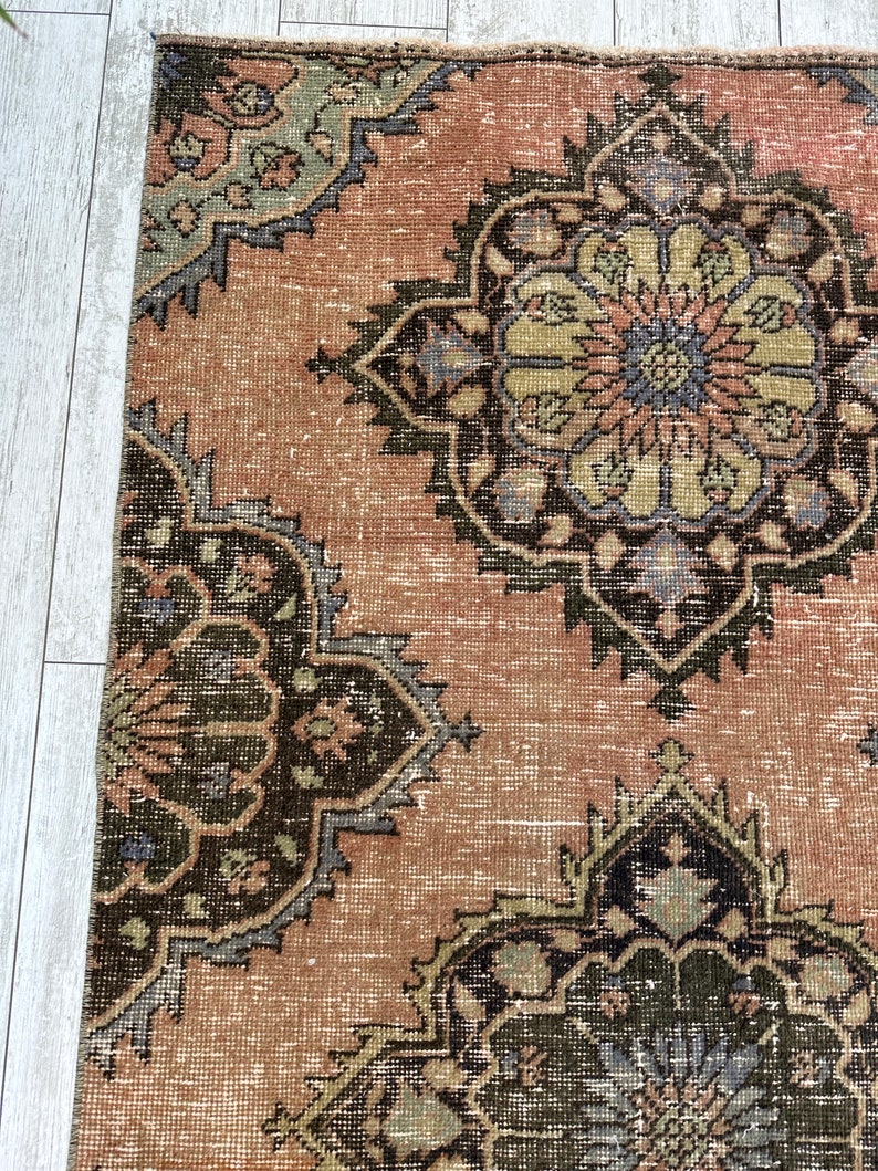 Puede incluir: Una alfombra vintage con un fondo rosa descolorido y intrincados patrones florales en tonos de verde, marr&oacute;n y azul.
