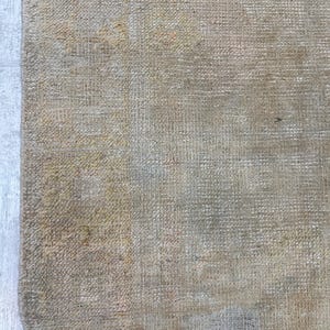 May include: Close-up of the back of a woven rug with a beige and brown color scheme. The rug has a textured surface and a slightly faded appearance.