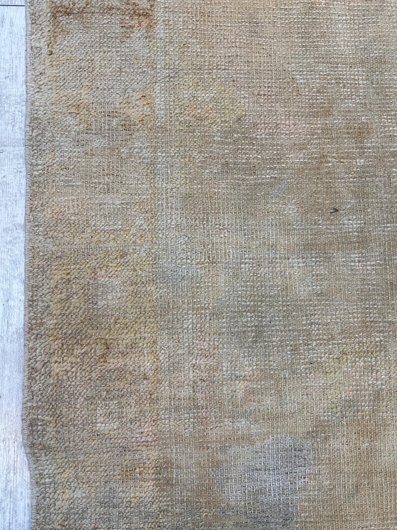 May include: Close-up of the back of a woven rug with a beige and brown color scheme. The rug has a textured surface and a slightly faded appearance.
